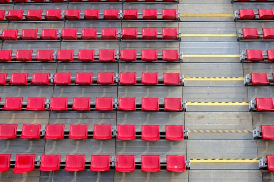 High angle view of rows of empty red plastic seats and concrete stairs with yellow safety hazard stripes in an outdoor sports stadium arena