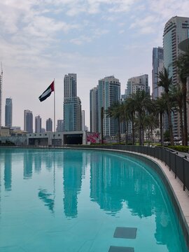 Bandera de los Emiratos &Aacute;rabes Unidos frente a rascacielos modernos con reflejo en el agua