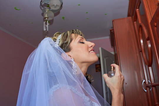 Beautiful bride applying perfume on her neck on wedding morning, Side view of bride spraying luxury perfume close up