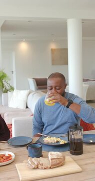 Vertical video: African couple sharing breakfast at home, man finishing juice and sliding glass
