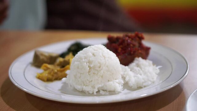 A plate of Nasi Padang with beef tendon curry, green chili paste, and cassava leaves, a traditional Indonesian dish.