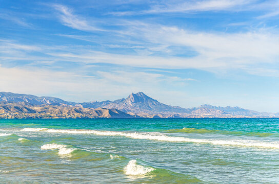 Mediterranean Sea azure water with waves in sunny summer day, White Coast Costa Blanca coastline with Puig Campana mount of Prebaetic System mountain range background, Valencian Community, Spain