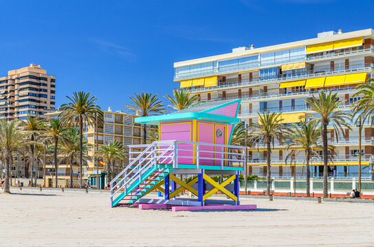 Playa de San Juan beach in Alicante city, colorful Lifeguard Hut Lifeguard Tower on sandy beach of Mediterranean Sea coast in sunny summer day, multistory residential buildings background, Spain