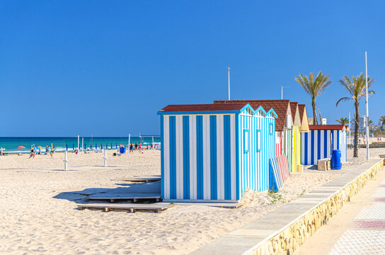 Playa de San Juan beach in Alicante city embankment, colorful striped bathing huts sheds cabins on Muchavista sandy beach of Mediterranean Sea coast Costa Blanca coastline in sunny summer day, Spain