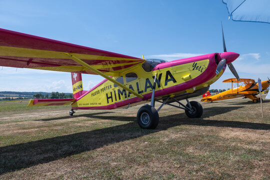 Grenchen, Switzerland - 11.07.2026: Brightly painted propeller aircraft displayed on grass at an airfield event under blue sky.