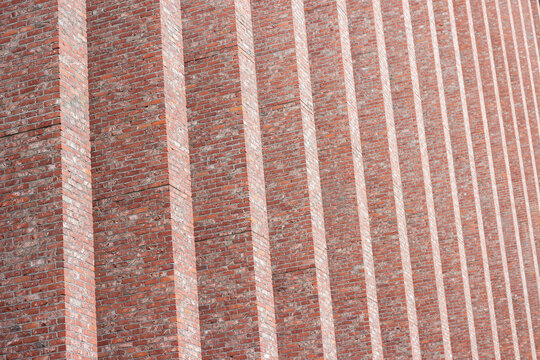 Textured red brick wall with vertical lines and shadows creating a geometric pattern, showcasing the craftsmanship of masonry in an urban architectural setting