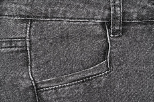 Closeup detail of black denim jeans fabric. Features front pocket, waistband seam and belt loop. Neutral textile background for fashion, apparel concepts, and clothing industry design