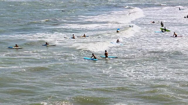 Pull-back shot from a distant view of a surf school session on Cromer Beach, North Norfolk coast. The camera reveals surfers practising in the waves, with a wide coastal landscape under a bright sky.