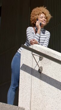 Vertical video: Leaning woman wearing striped top starting call on parapet, laughing, reading phone