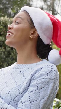 Vertical video: Entering helper hand adjusting Santa hat in garden, woman turning head and smiling