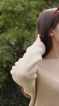 Vertical video: Lifting arm, woman fixing red headband tucking at hedge in tan jumper, copy space