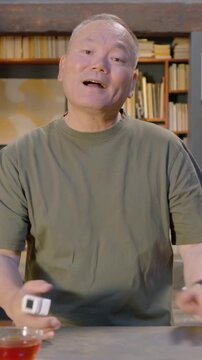 Vertical video: Smiling and speaking, senior man demonstrating white device at home study