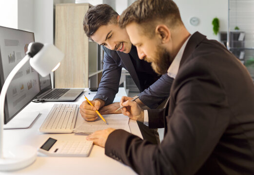 Accountants analysts perform finance analysis with teamwork. Two colleagues review data, write notes, and calculate figures for budgets. Cooperative workflow supports accurate financial decisions.