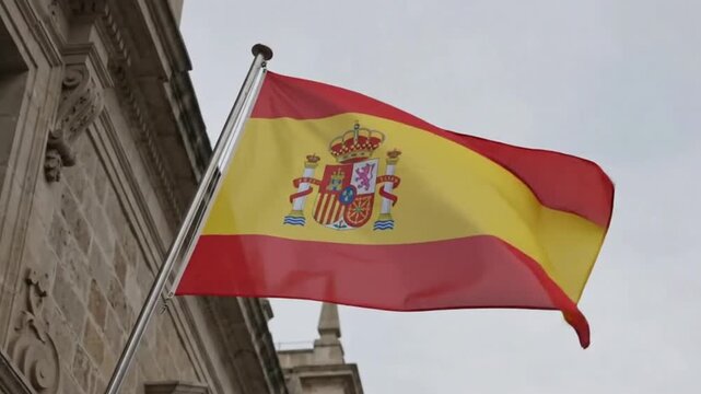 National flag of spain waving in the wind against a stone building background