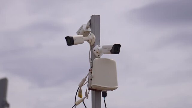 Multiple white cctv cameras mounted on a metal pole providing outdoor surveillance and monitoring against a cloudy sky, with the flag of georgia visible in the background