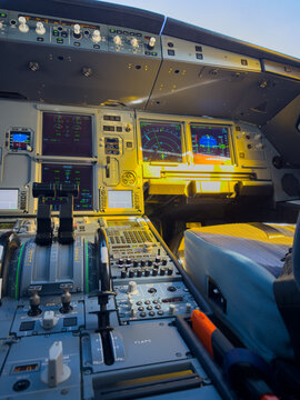 Detailed view of a modern airliner cockpit instrument panel showing glass displays, thrust levers, sidestick and flight controls
