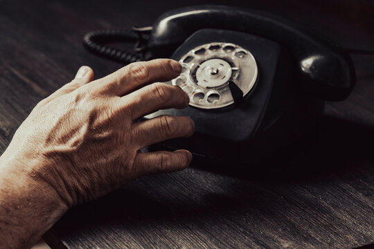 Man hand dialing on vintage black rotary telephone, closeup. An elderly man hand dialing an old black rotary telephone on dark rustic wooden table background