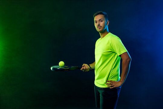 Padel tennis player with racket. Man athlete with paddle racket on court with neon colors. Sport concept. Download a high quality photo for the design of a sports app or betting site.