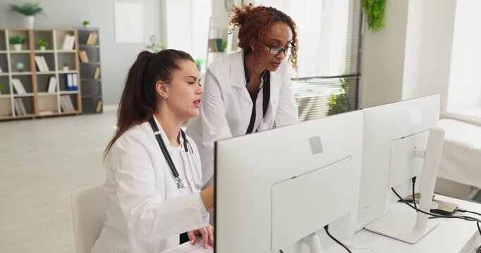 Doctors team using computer for healthcare records analysis. In a clinic physicians collaborate at monitors reviewing patients data. Concept: digital consultation and diagnosis workflow.