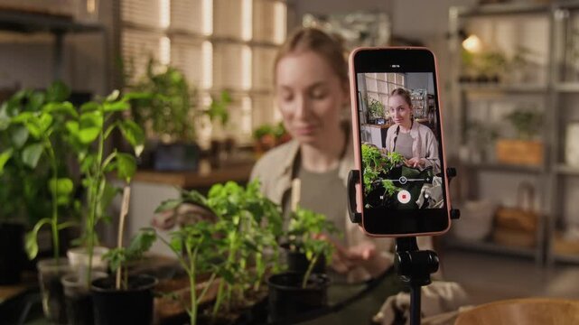 Young Caucasian woman recording gardening vlog on smartphone mounted on tripod. Footage perfect for social media marketing, content creation, and online education campaigns