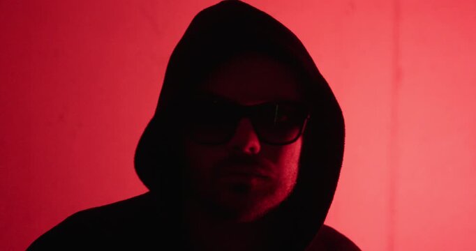 Silhouette of a hooded man in dramatic red lighting, representing anonymity, cybercrime, mystery, and digital security concepts.