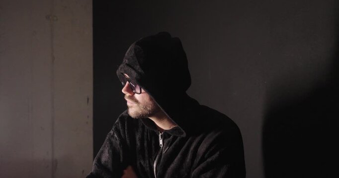 Hooded man cautiously looking left, right, and then directly into the camera, representing suspicion, surveillance, cybercrime, and security threats.