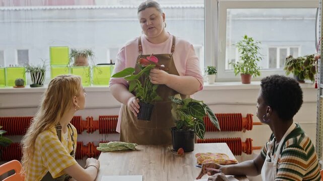 Caucasian female instructor teaching diverse young adult women about plant care during workshop. Video is perfect for promoting educational classes or small business training, medium shot
