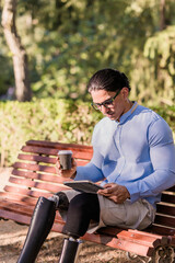 Fototapeta premium Latino man with prosthetic legs enjoying coffee break in park