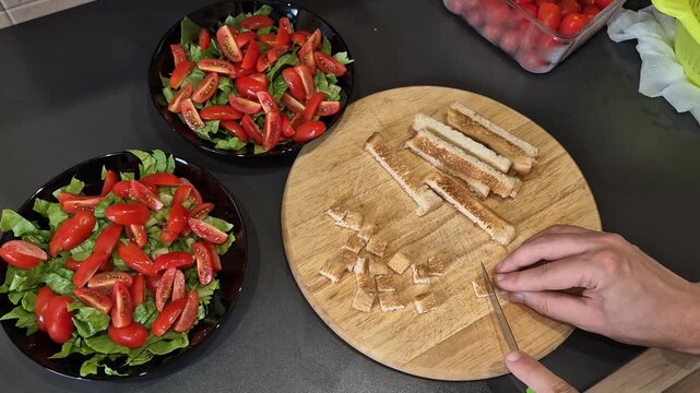 Preparing chicken caesar salad by slicing bread on wooden cutting board