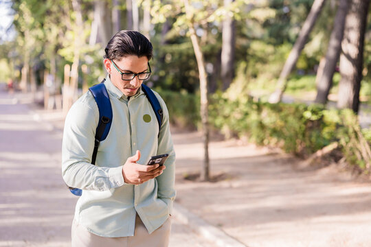 Latino man with backpack using smartphone in park