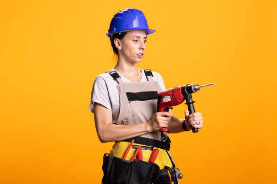 Woman contractor uses drill gun, demonstrating practical DIY and repair abilities. Female builder appears to drill into imaginary wall in studio, representing work on construction project.