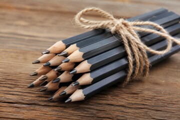 Naklejka premium Bundle of Black Wooden Pencils Tied with Twine on Rustic Wooden Surface