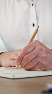 Hands of a male wearing white shirt taking notes into the paper book. Close up view of a handwriting with a ball pen. Vertical video