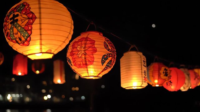 A string of illuminated, patterned paper lanterns glowing against the dark night sky