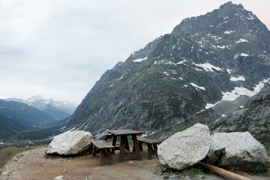 Wooden picnic table on a scenic mountain ledge overlooking rugged peaks and a valley under a cloudy alpine sky