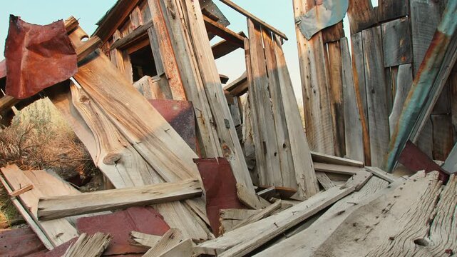Old abandoned ghost town in America featuring collapsed wooden building with weathered planks and rusty metal sheets. Decaying structure shows broken timber and debris in arid desert landscape.