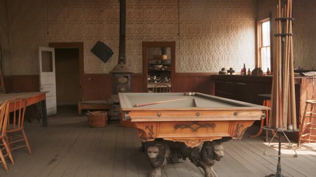 Old abandoned ghost town in America featuring vintage billiard room with ornate pool table and lion claw feet. Antique cast iron stove and wooden chairs create authentic western atmosphere.