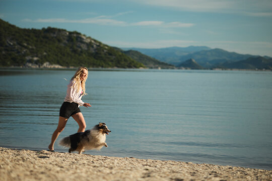 A woman runs together with her Shetland Sheepdog along a peaceful lakeshore. Active outdoor lifestyle scene promoting fitness, companionship, travel, and healthy living.