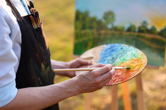 Man painting beautiful landscape on canvas, closeup. Artist working outdoors