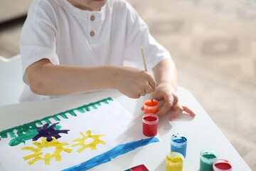 Little boy drawing picture with paints and brush at white desk indoors, closeup. Space for text © New Africa