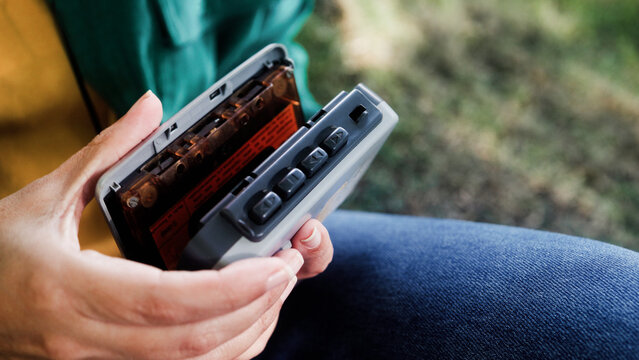 Person inserting cassette tape into portable player outdoors - Retro audio and nostalgia lifestyle trend