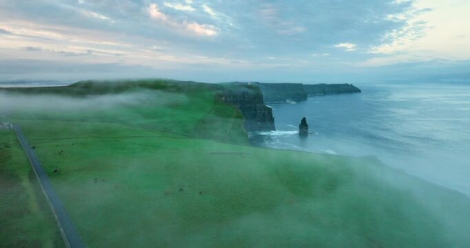 Drone flying along Cliffs of Moher with sea stack and drifting fog at sunrise