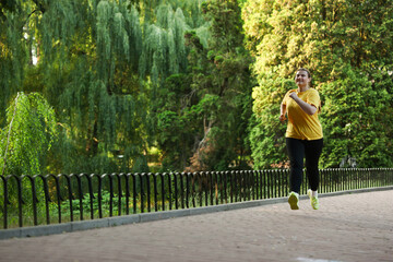 Obraz premium Smiling overweight woman running in park. Space for text