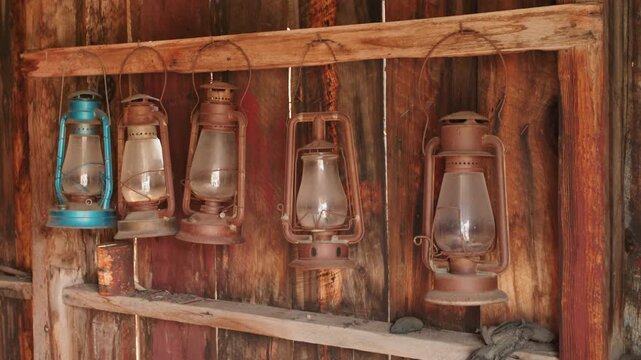 Old abandoned ghost town in America featuring collection of vintage kerosene lanterns hanging on rustic wooden rack. Weathered oil lamps with glass globes displayed against aged barn wood planks.