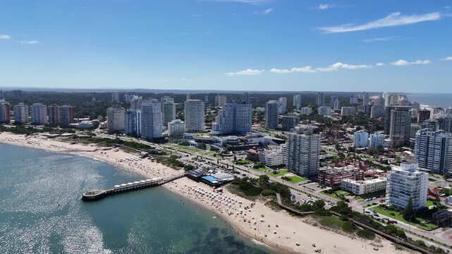 Drone view of Mansa Beach, the iconic wooden pier, turquoise waters and the modern skyline of Punta del Este on a sunny summer day in Uruguay.