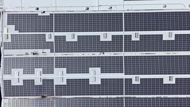 Rows of solar panels are installed on the roof of a big building in a city. This setup represents a move toward using clean energy and reducing reliance on fossil fuels