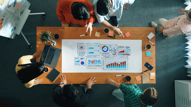 A diverse team engages in a strategic business meeting discussing data visualizations and charts on a wooden table, showcasing collaboration and creativity in a modern office. Trope