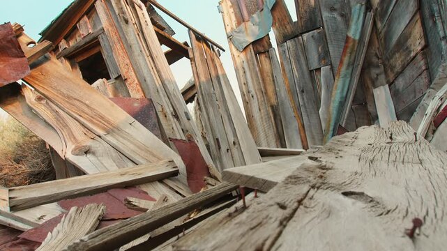 Low angle perspective reveals collapsed wooden building ruins with weathered gray timber planks scattered chaotically, rusty corroded metal sheets.