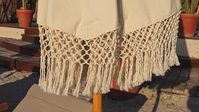 Close up footage of a handmade white macrame fringe wall hanging displayed outdoors in natural sunlight, showing intricate knotted patterns and hanging textile details.