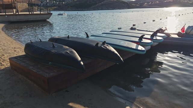 Close view of rowing boats and canoes moored side by side at a calm lake waterfront with sunlight gleaming on the water